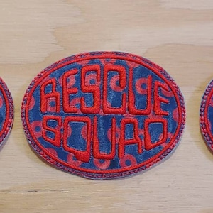 Può includere: Tre toppe rotonde ricamate in blu e rosso con il testo "RESCUE SQUAD" in rosso.