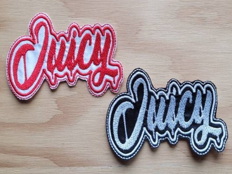 May include: Two embroidered patches with the word "Juicy" in a stylized font. The top patch is red with white outlining, and the bottom patch is black with silver outlining.