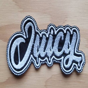 May include: A white embroidered patch with the word "Juicy" in black lettering.