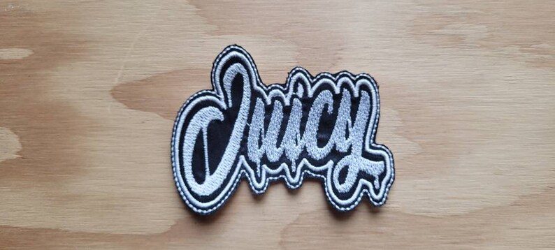 May include: A white embroidered patch with the word "Juicy" in black lettering.
