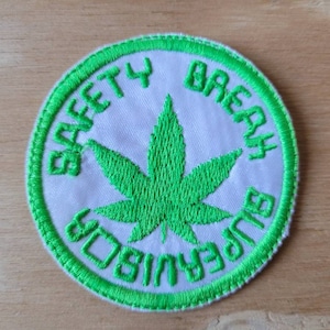 May include: Green embroidered patch with a white background and the text "Safety Break Supervisor" around a green marijuana leaf.