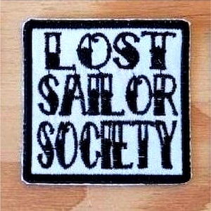May include: Black and white embroidered patch with the text "LOST SAILOR SOCIETY" on a white background.