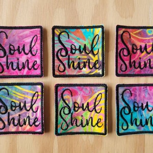 May include: Six colorful square fabric patches with black stitching around the edges. Each patch has a white background with a colorful abstract design and the text "Soul Shine" in black cursive lettering.