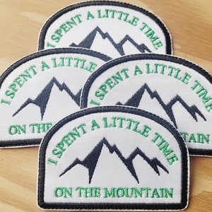 May include: Four embroidered patches featuring a mountain design. Each patch is white with a black and green mountain graphic and the text "I SPENT A LITTLE TIME ON THE MOUNTAIN" in green lettering. The patches have a black border.