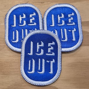 Op de afbeelding: Drie blauwe geborduurde patches met de woorden "ICE OUT" in witte blokletters. Elke patch heeft een witte rand en een afgeronde rechthoekige vorm. De patches zijn in een cluster gerangschikt.