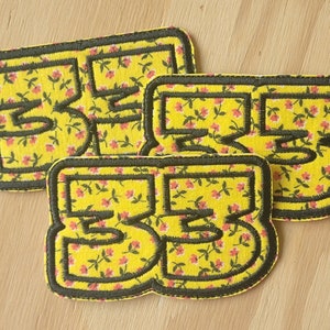 May include: Three iron-on patches with black outlines and a yellow floral pattern. The patches feature the numbers "2", "3", and "5" in black.
