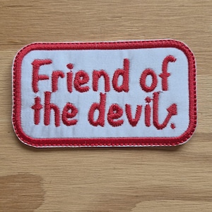 May include: White embroidered patch with red stitching. The patch reads "Friend of the devil."