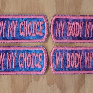 May include: Four pink and blue fabric patches with the text "MY BODY MY CHOICE" embroidered in white.