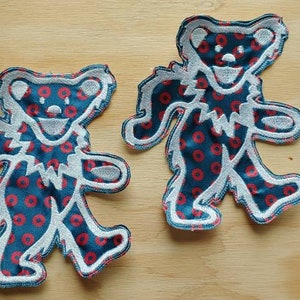 May include: Two blue and red fabric patches of dancing bears with a white outline. The bears are wearing a pattern of red circles on a blue background.