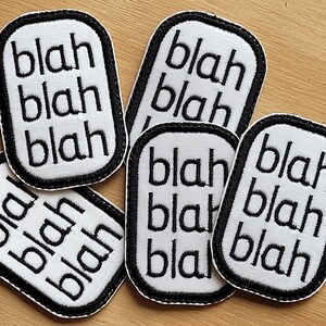 May include: Six white fabric patches with black stitching and the word "blah" repeated three times on each patch.