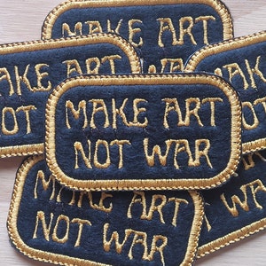 May include: A stack of five black felt patches with gold embroidered edges. Each patch reads "Make Art Not War".