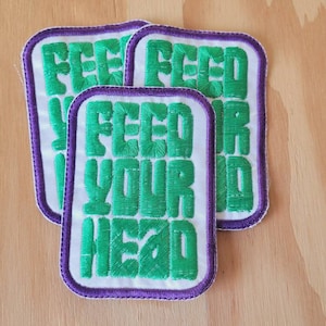 May include: Three white and green embroidered iron-on patches with purple stitching. Each patch reads "Feed Your Head".