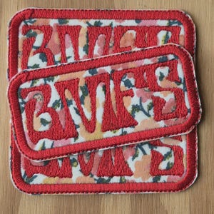 May include: Two rectangular embroidered patches with the word "BVES" in red, outlined with red stitching. The patches feature a floral pattern background and a red border. The patches have rounded corners.