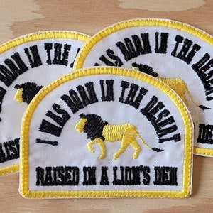 May include: Three white fabric patches with yellow trim and black embroidery. The patches read "I Was Born In The Desert Raised In A Lion's Den".