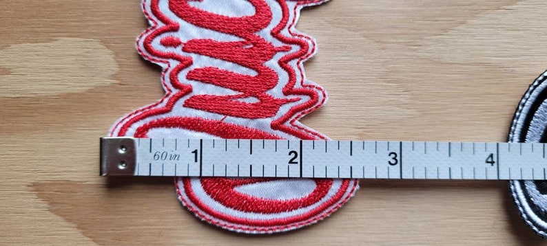 May include: Red embroidered patch with the word "S**" in a stylized font. The patch is approximately 2 inches wide and 1 inch tall.