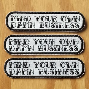 May include: Three white fabric patches with black embroidered text that reads "Mind Your Own Damn Business".