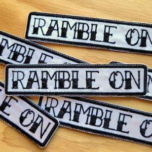 May include: Five white fabric patches with black embroidered text that reads "Ramble On".