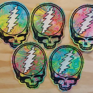 Op de afbeelding: Vijf kleurrijke tie-dye patches met een schedel met een bliksemontwerp. De patches zijn rond en hebben een zwarte omtrek.