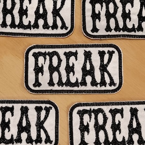 Könnte beinhalten: Fünf weiße Stoff-Patches mit schwarzen gestickten Buchstaben, die "FREAK" lesen.
