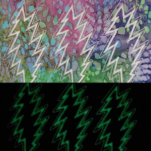 Puede incluir: Primer plano de un parche de tela con un patr&oacute;n tie-dye y un dise&ntilde;o de rayo blanco bordado. El parche est&aacute; sobre un fondo negro con un dise&ntilde;o de rayo verde que brilla en la oscuridad.