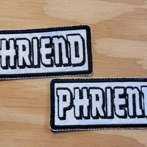 May include: Two white embroidered patches with black outlines. Both patches say "PHRIEND" in a stylized font.