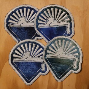 May include: Four blue and white embroidered patches with a white cat silhouette lying on a white triangle with a white sunburst behind it.