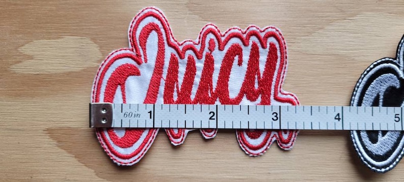 May include: Red embroidered patch with the word "Juicy" in white outlined letters. The patch is about 3 inches wide and is measured with a ruler.