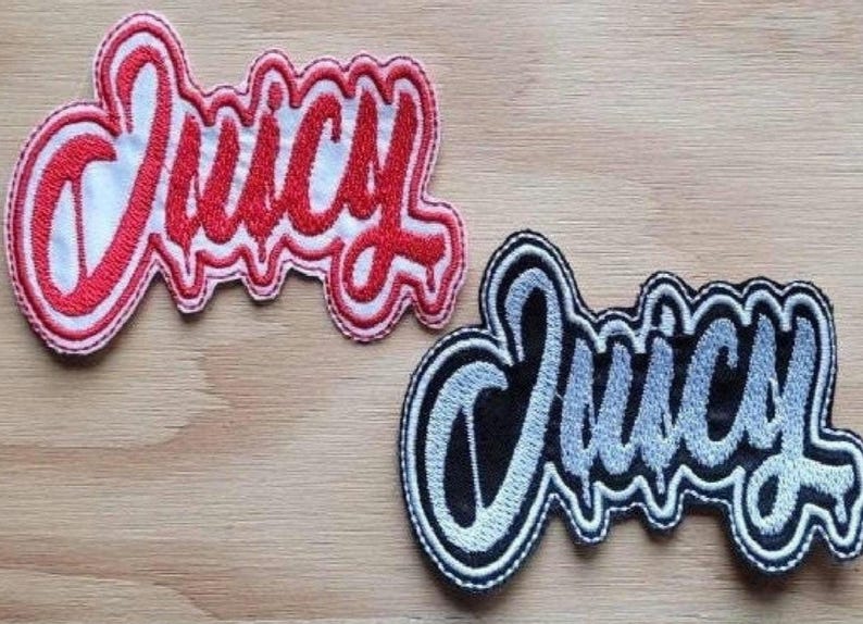 May include: Two embroidered patches with the word "Juicy" in a stylized font. The top patch is red on white fabric, and the bottom patch is silver on black fabric.