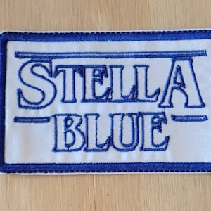 May include: White embroidered patch with blue stitching. The patch says "STELLA BLUE" in a stylized font.