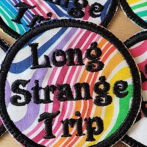 May include: A round, colorful patch with a black border and the text "Long Strange Trip" in black embroidery.