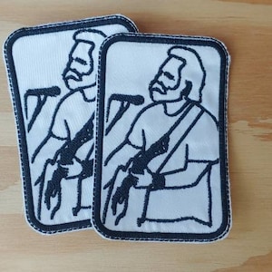 Könnte beinhalten: Zwei weiße gestickte Aufnäher mit schwarzen Umrissen einer Person, die Gitarre spielt. Die Aufnäher haben einen weißen Hintergrund und schwarze Nähte.