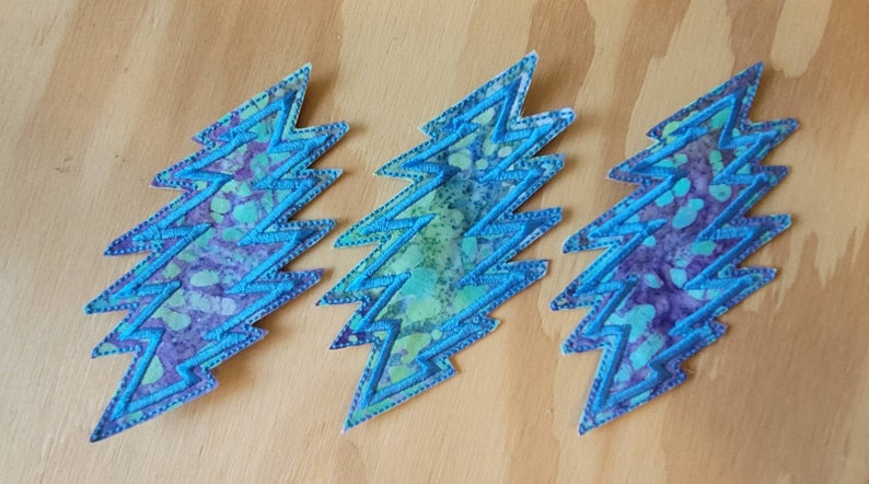 Puede incluir: Tres parches de rayo azul y morado con estampado tie-dye y costuras blancas.