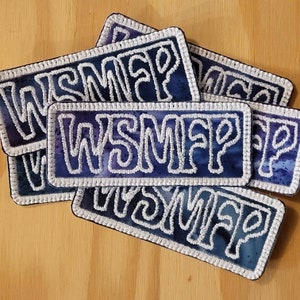 Peut inclure: Six patchs brodés de couleur violette et blanche avec le mot "WSMAP" écrit en blanc sur chaque patch.