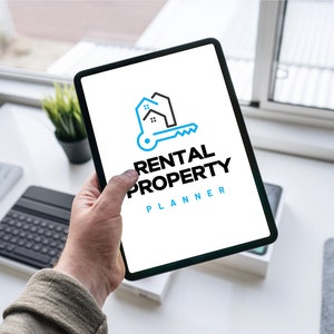 May include: A white tablet with a black border displays a logo for a rental property planner. The logo is a blue and black illustration of a house with a key. The text "Rental Property Planner" is below the logo.