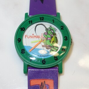 May include: Green and purple wristwatch with a cartoon turtle on the face. The watch face says "Funimals Bandit".