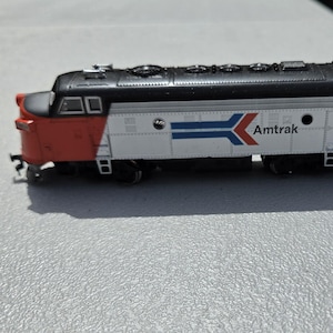 May include: A model Amtrak train engine, featuring a red front, white and silver body, and a black roof. The Amtrak logo is displayed on the side, along with the number 505. The miniature train is a detailed replica.