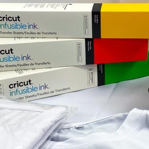 May include: Three packages of Cricut Infusible Ink Transfer Sheets. Each package is a different color: yellow, red, and green. The packages are stacked on top of each other. The text on the packages reads "Cricut Infusible Ink. Transfer Sheets/Feuilles de Transferts".