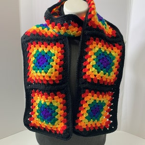May include: A black crocheted scarf with rainbow granny squares. The scarf is made with black yarn and features four colorful squares with a rainbow pattern.