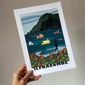 May include: A colourful illustration of a seaside town with a large cliff in the background. The illustration features several boats in the water, a person standing on a pier, and a field of orange flowers in the foreground. The text "ILFRACOMBE" is printed at the bottom of the illustration.