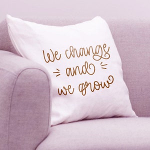 K&ouml;nnte beinhalten: Ein wei&szlig;es Kissen mit dem Text "We change and we grow" in brauner Kursivschrift.