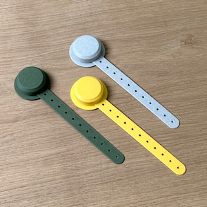 Op de afbeelding: Drie meetlinten met verschillende gekleurde uiteinden: grijs, geel en groen. Elk lint heeft een cirkelvormig uiteinde met een nummerenschaal gemarkeerd in inches.