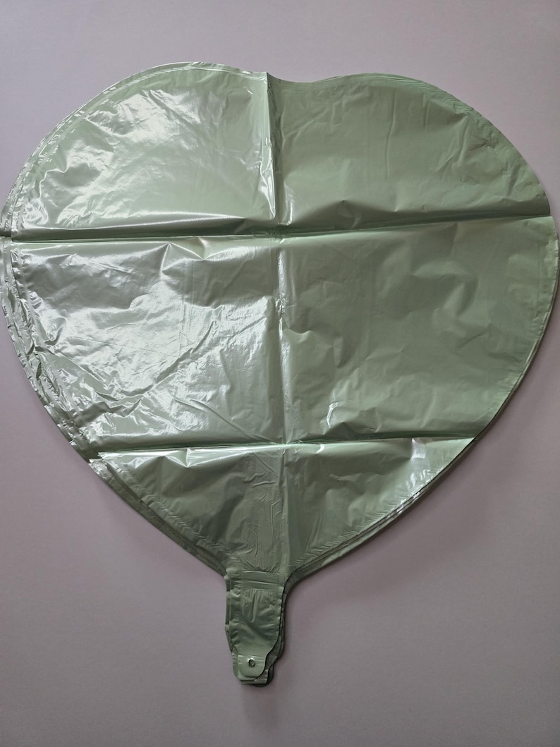 Op de afbeelding: Een grote, hartvormige ballon in een gedempte groene kleur. De ballon is gemaakt van een glanzend, gekreukt materiaal en heeft een gevouwen basis met een kleine, knoopachtige sluiting. De ballon is ontworpen voor feesten en evenementen.