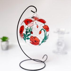 May include: A glass bauble with a black metal stand, featuring hand-painted red poppies with green leaves and stems. The bauble has a dotted pattern.
