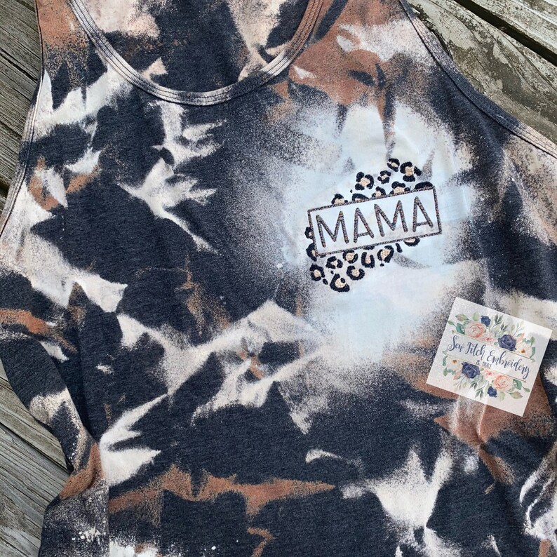 May include: A black and white tie-dye tank top with a brown and white leopard print design. The word "MAMA" is embroidered in a white rectangle with a black outline.