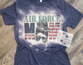 May include: A blue t-shirt with a bleached design featuring the text "Air Force Mom" with an American flag and a woman's face with a bun and sunglasses.