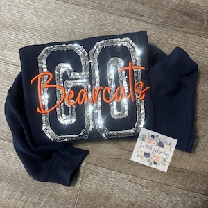 May include: Navy blue sweatshirt with a large sequined number "00" and the word "Bearcats" embroidered in orange.