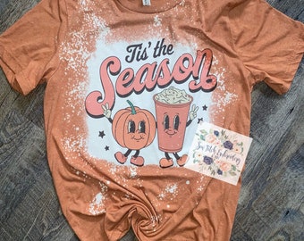 May include: A burnt orange t-shirt with a bleach-splattered design featuring a pumpkin and a cup of coffee with the text "Tis' the Season".