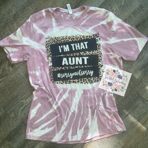 May include: A pink tie-dye t-shirt with a black and white graphic that says "I'm That Aunt #sorrynotsorry" with a leopard print border.