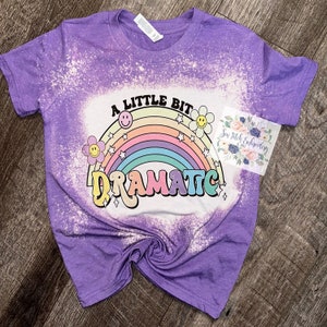 May include: Purple bleached t-shirt with a rainbow and the text "A little bit dramatic!" in a retro font.