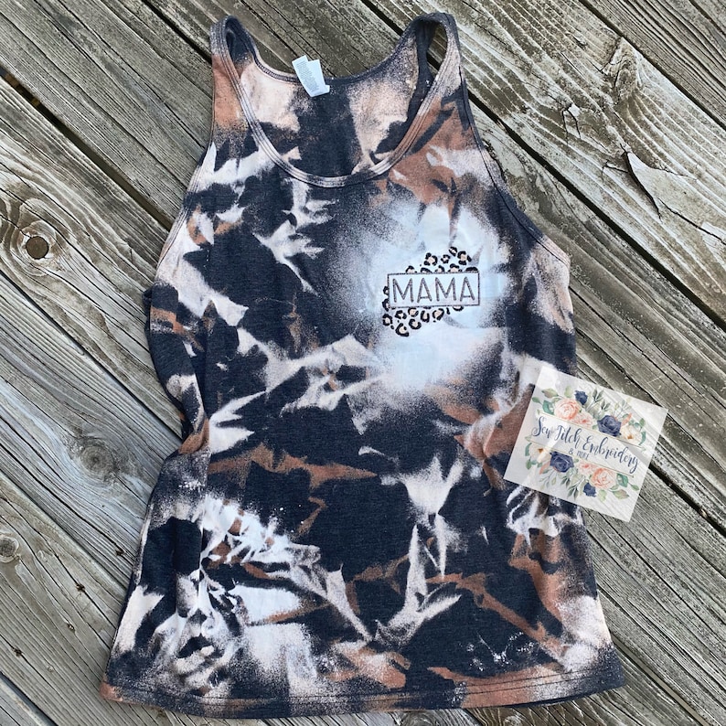 May include: A black and white tie-dye tank top with a white rectangle that says "MAMA" in black letters. The rectangle is surrounded by a leopard print design.
